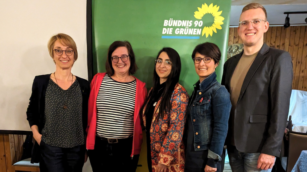 Tanja Josche, Eva Neubert und Henrik Schmidt-Heck mit Saghar Kia und Nina Afschari vor einem Banner von Bündnis 90/Die Grünen. Sie befinden sich in einem Innenraum mit einer gemütlichen Holzvertäfelung nach dem Vortrag.